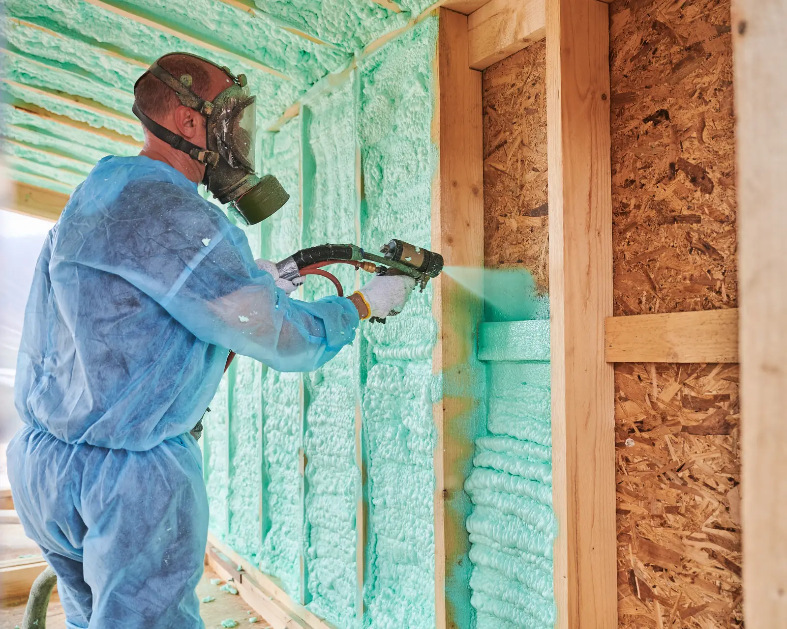 Applicator spraying green polyurethane foam insulation between wooden wall studs