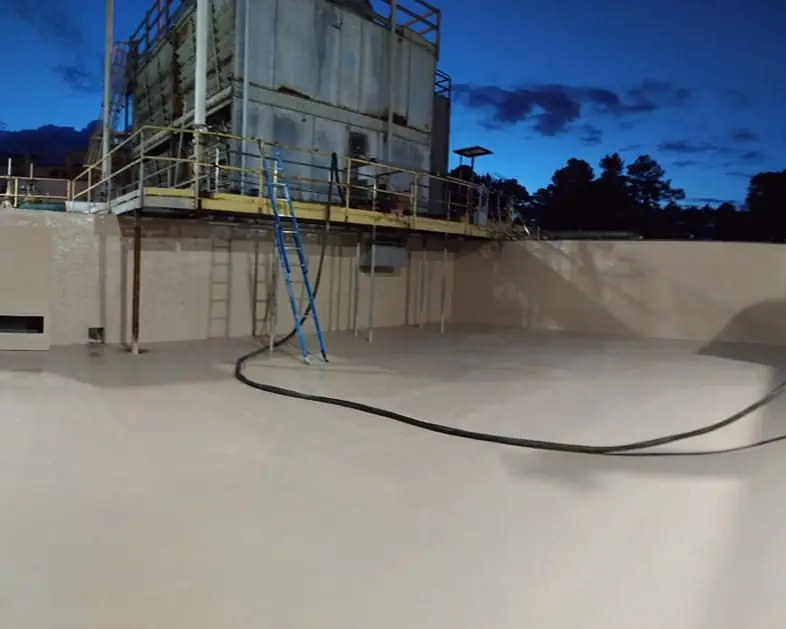 Applicator spraying a gray polyurea lining inside an open concrete tank at dusk